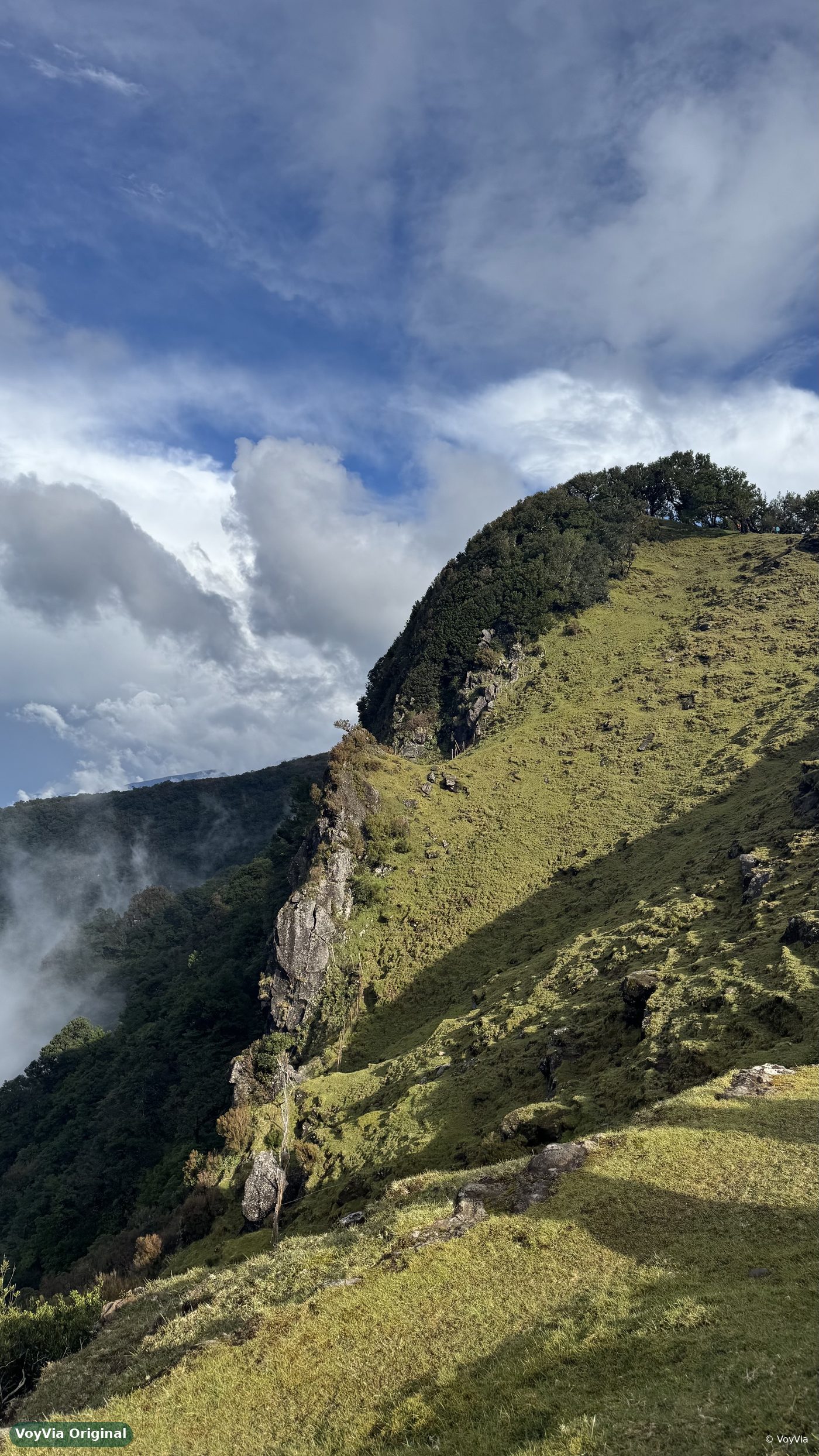 A steep green mountain ridge with rocks and low clouds on Madeira, Portugal.