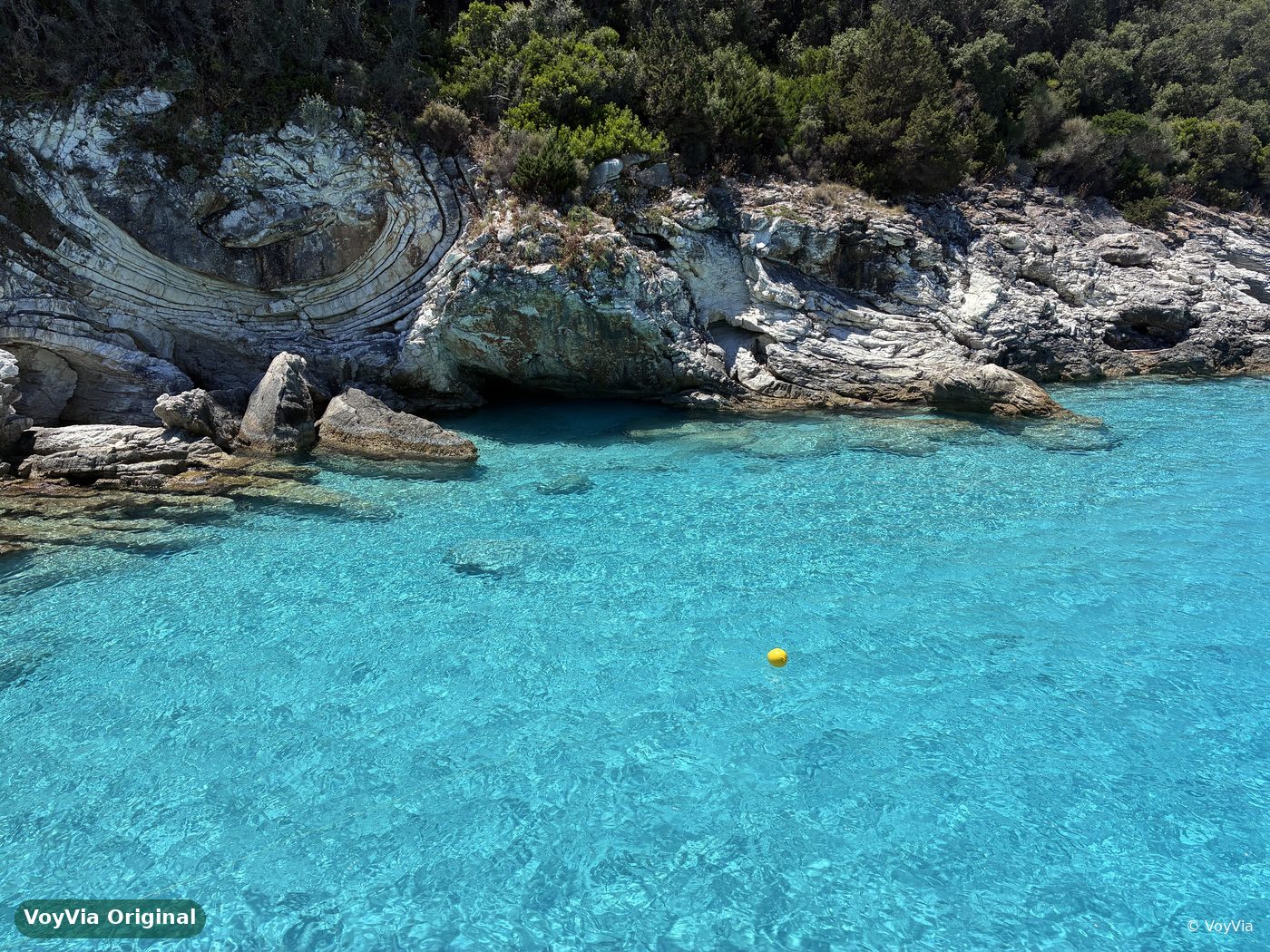Layered white rocks at the edge of crystal-clear turquoise water on Paxos, Greece.
