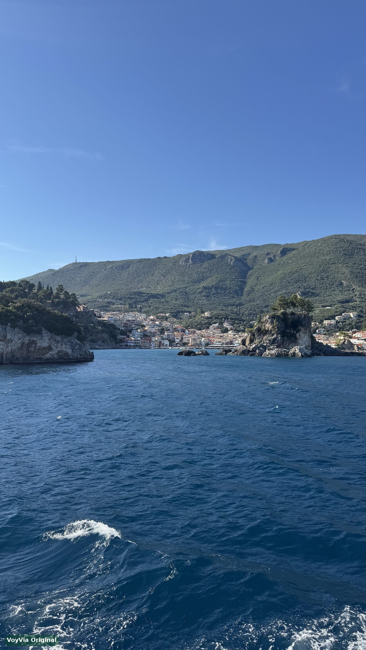 The coastal town of Parga in Greece seen from the sea, with green hills behind it.
