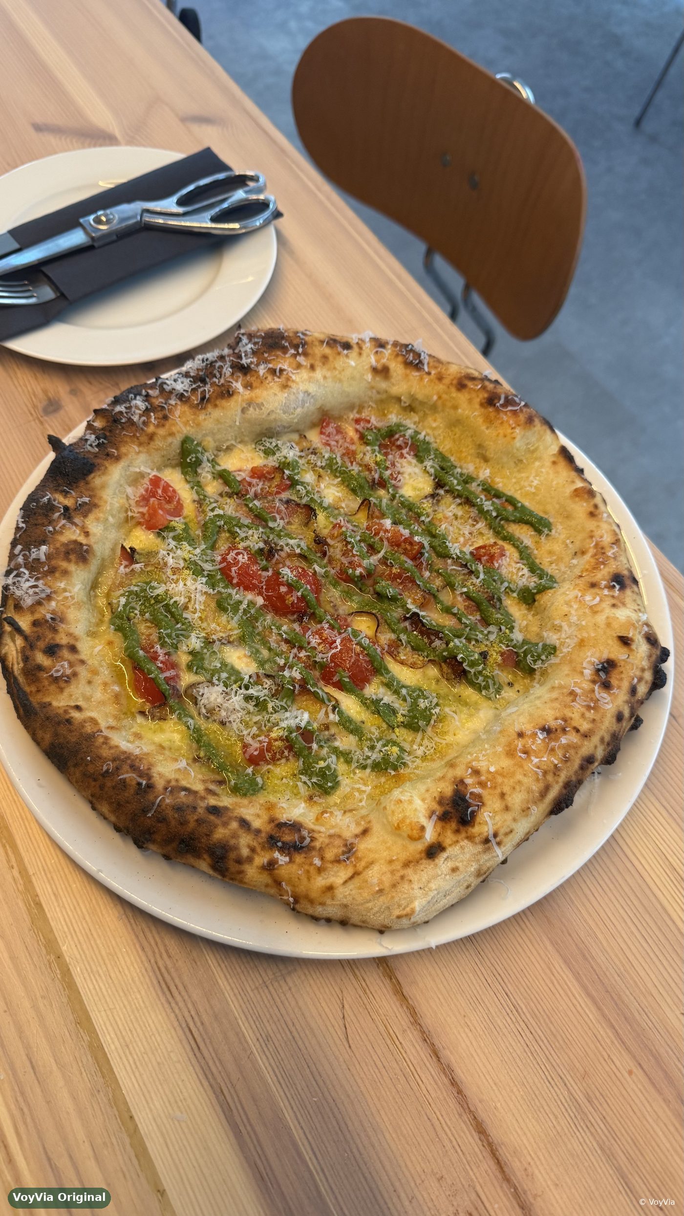Neapolitan-style pizza topped with cherry tomatoes, pesto and grated cheese on a plate.